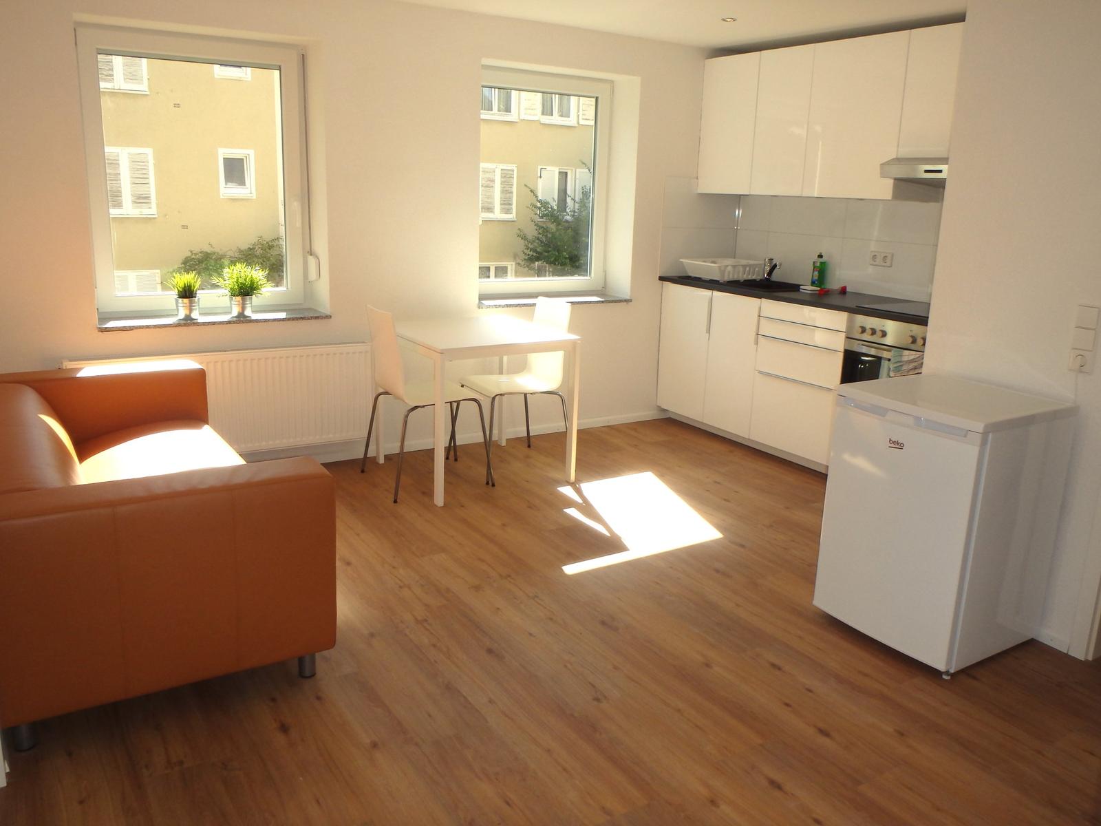 Sonniger Wohnbereich mit Sofa, Esstisch und weißer Einbauküche